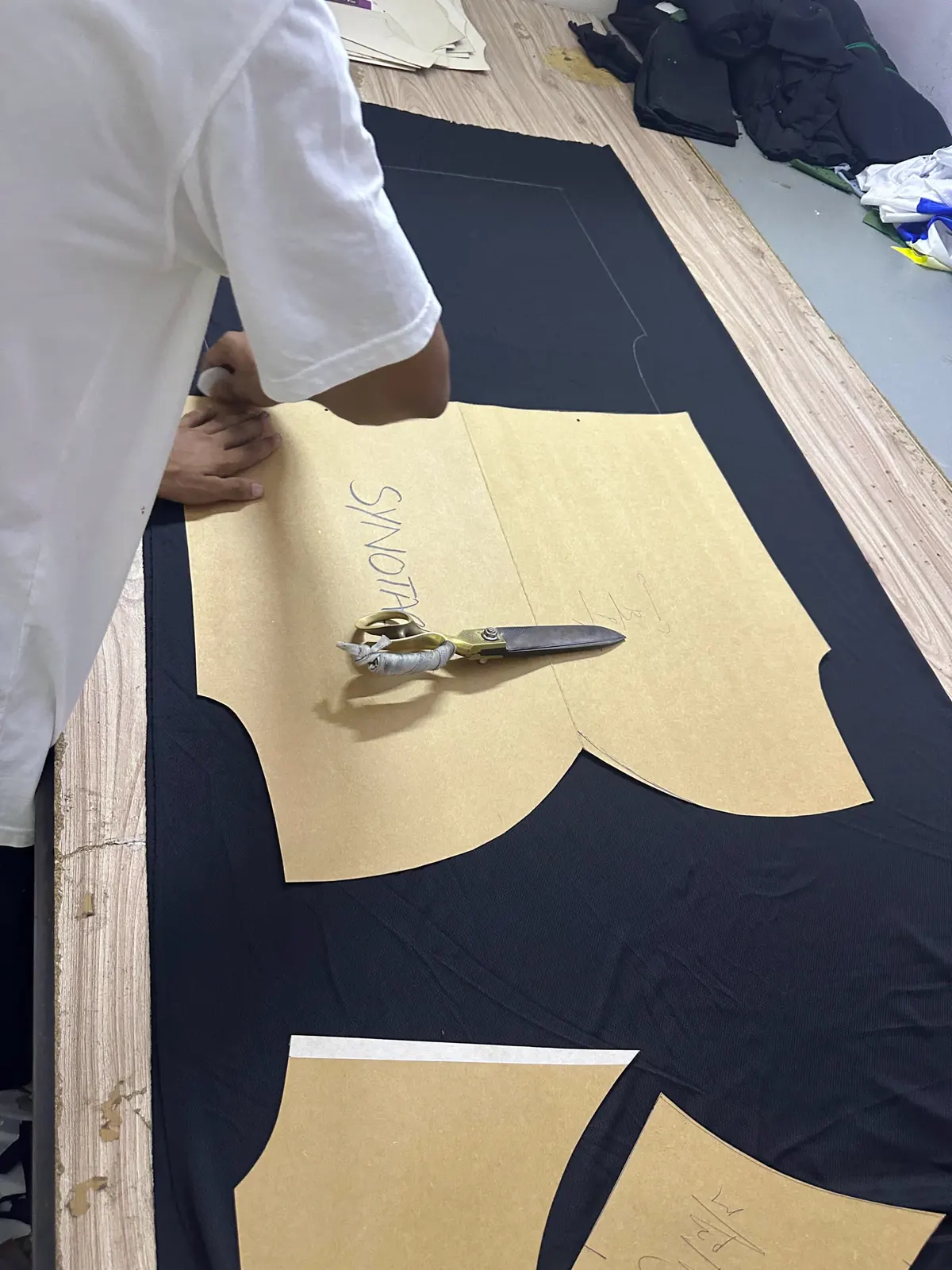A paper pattern marked Synotacy laid on black cloth, with tailor's shears, during cutting.